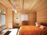 A tastefully spare selection of vintage pieces accents the warm knotty pine in the master bedroom. The orientation of the room maximizes the picture window that replaced the original garage door. Campbell designed a closet in an alcove behind the wall at the head of the bed.