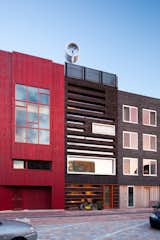 Along with the house's shou sugi ban front, the wood is layered with bright orange planks. Solar collectors, which consist of double-glass tubes that minimize heat loss, form a cornice on the front facade of the house. A wind turbine is on the roof.