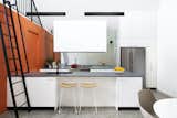 The kitchen features a mirrored backsplash that makes the space feel larger. The orange cabinetry conceals the laundry.